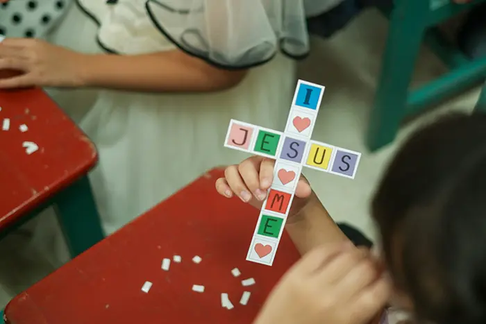 child holding paper cross with I heart Jesus and Jesus Hearts me